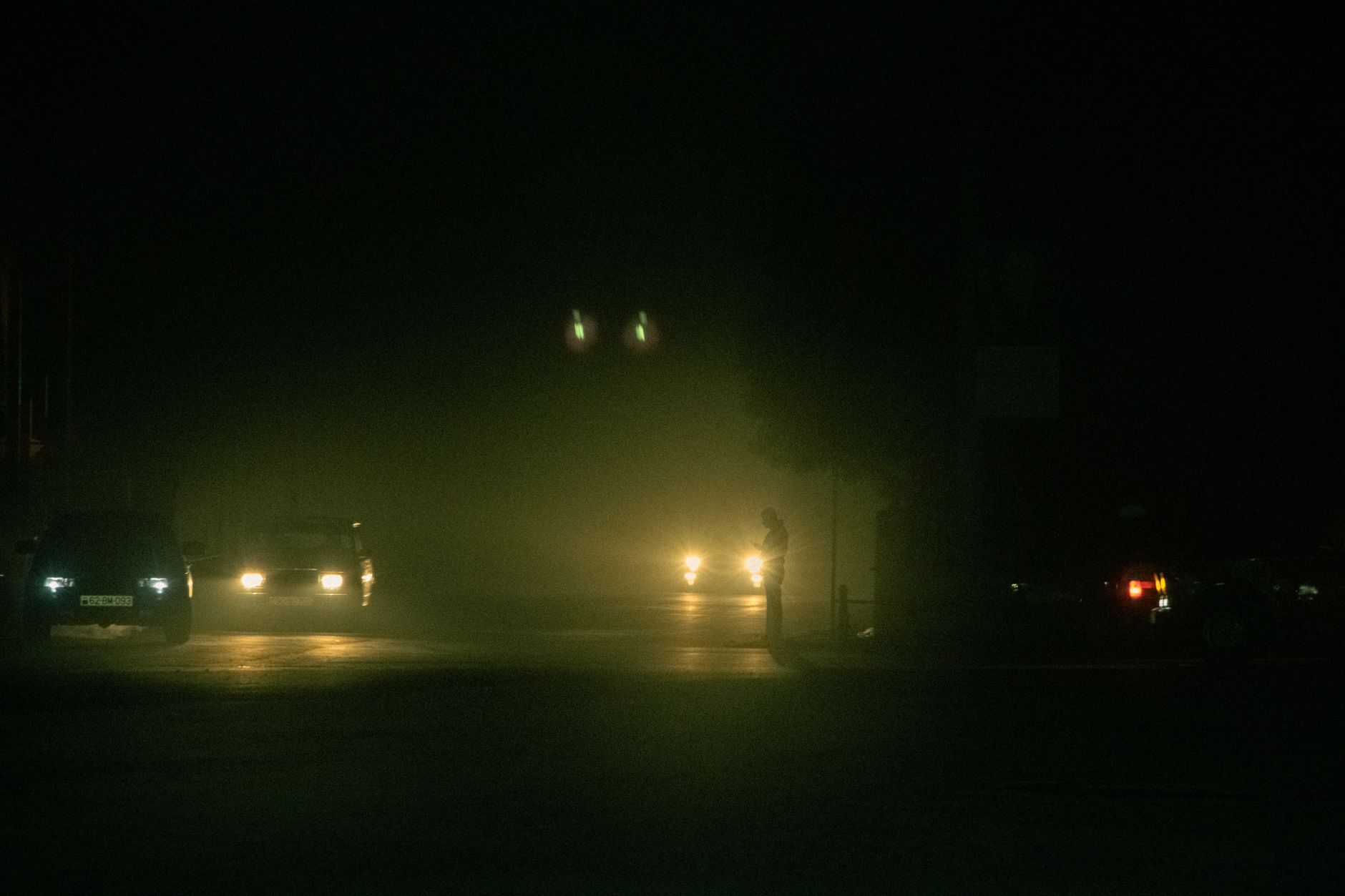 Dramatic night scene capturing cars and a silhouette on a foggy street.