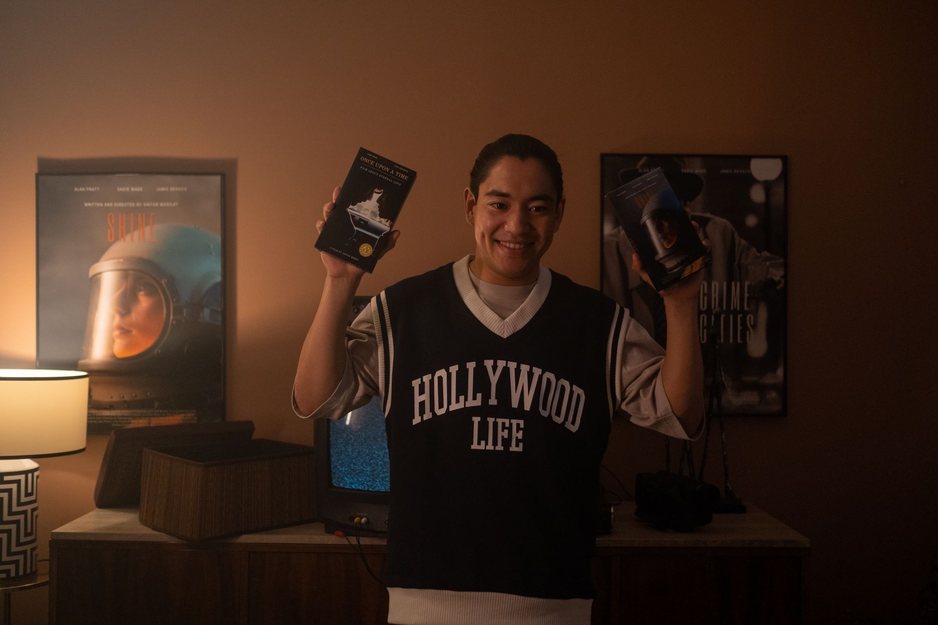 Smiling man holding vintage VHS tapes, standing in a warmly lit room