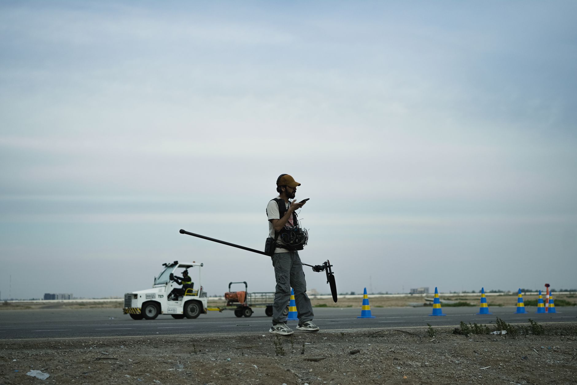Cameraman standing on road checking equipment while filming an outdoor scene.