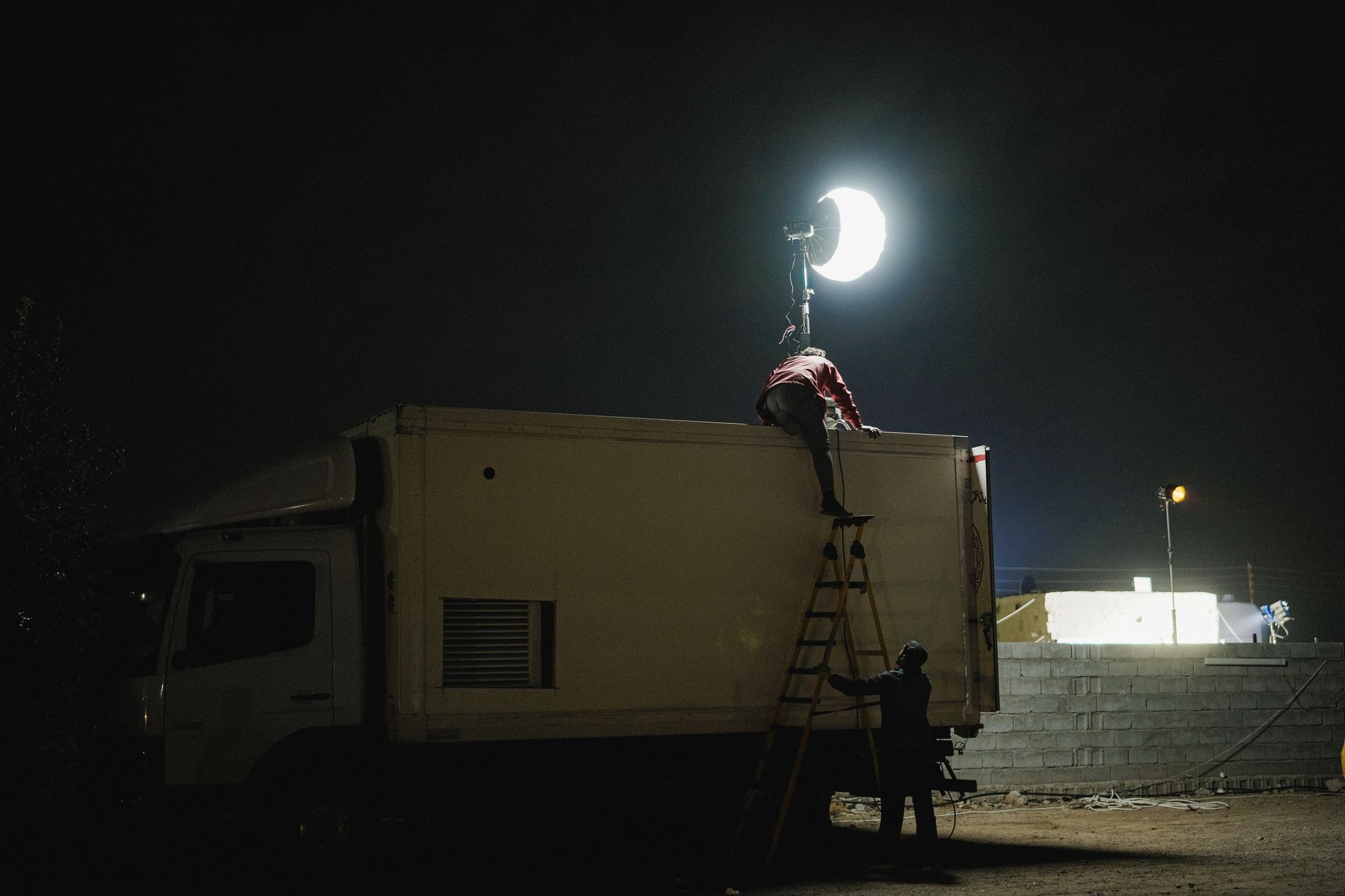 Film crew setting up lighting equipment on a truck at night for