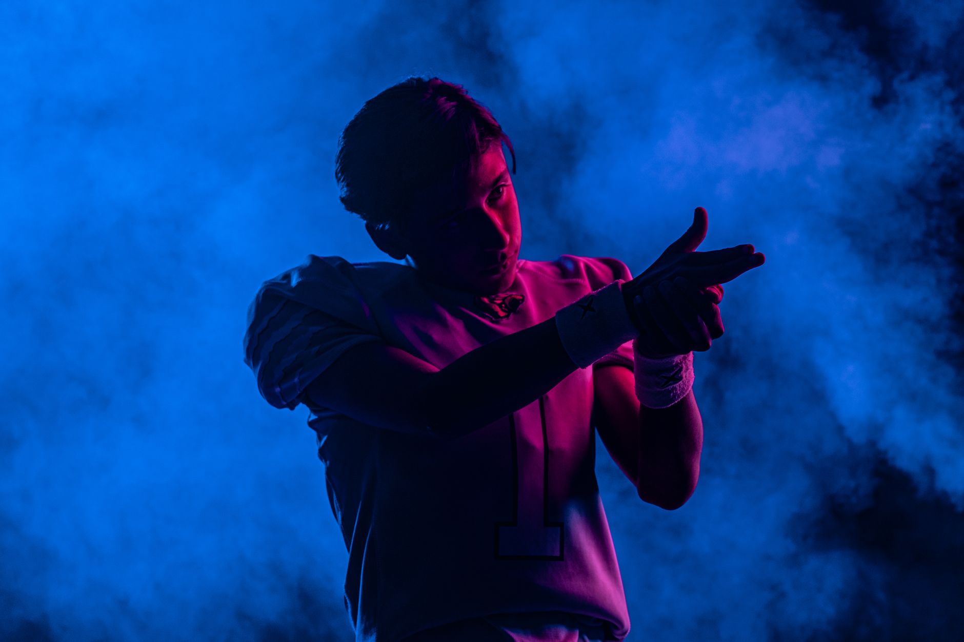 Silhouetted football player in colorful smoke with blue and pink lighting, dramatic