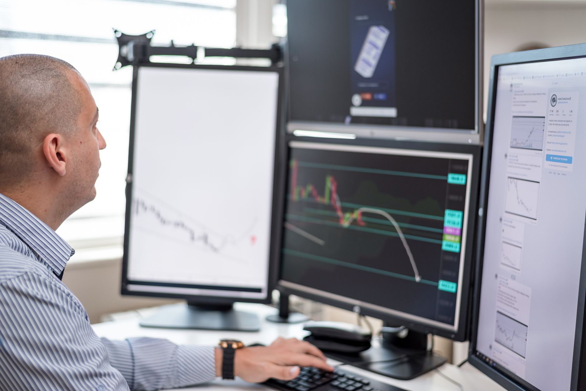 Stock trader analyzing financial graphs on multiple computer monitors in an office