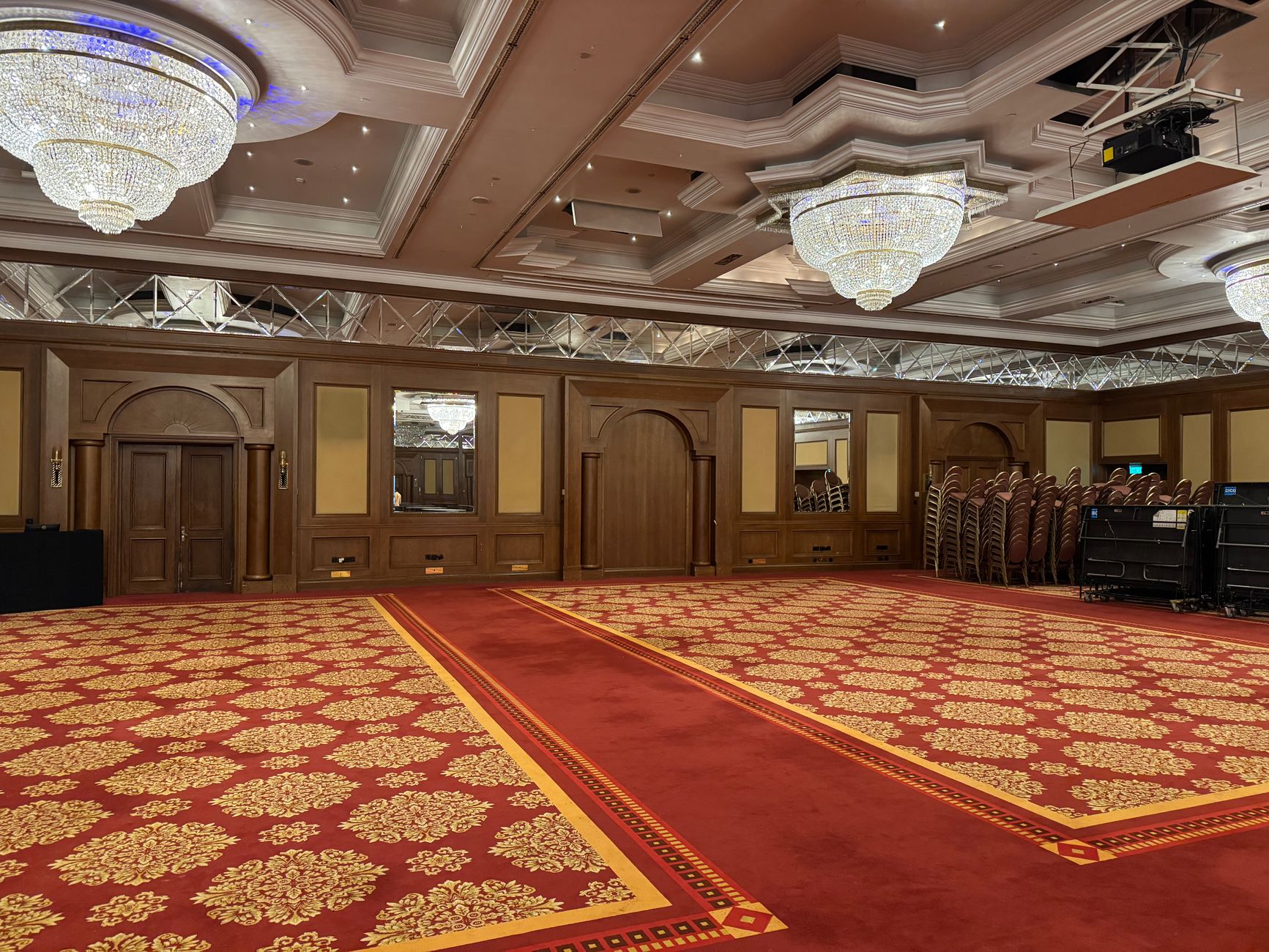 Spacious banquet hall with luxurious chandeliers and red carpet flooring.